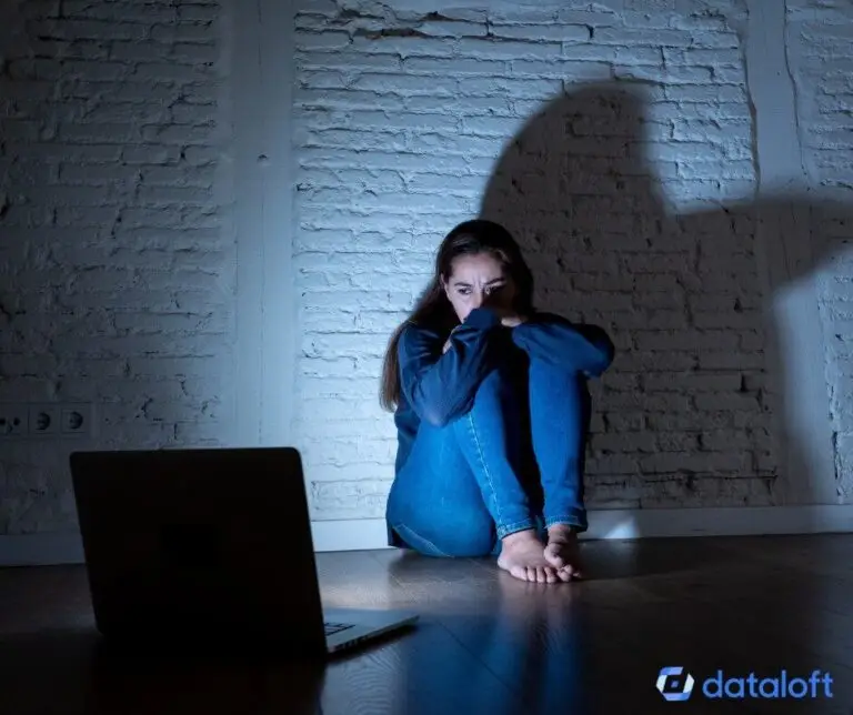 Frau kauert entfernt von ihrem Laptop an der Wand traurig ängstlich Opfer von Cybermobbing